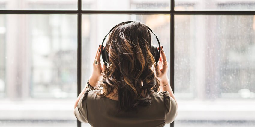 back of woman listening to music in front of window